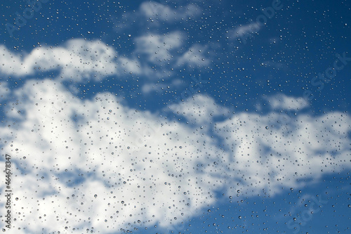 Raindrops on glass on a background of blue sky with clouds