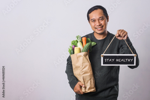 Man holding grocery shopping bag with vegetables and board that says Stay Healthy