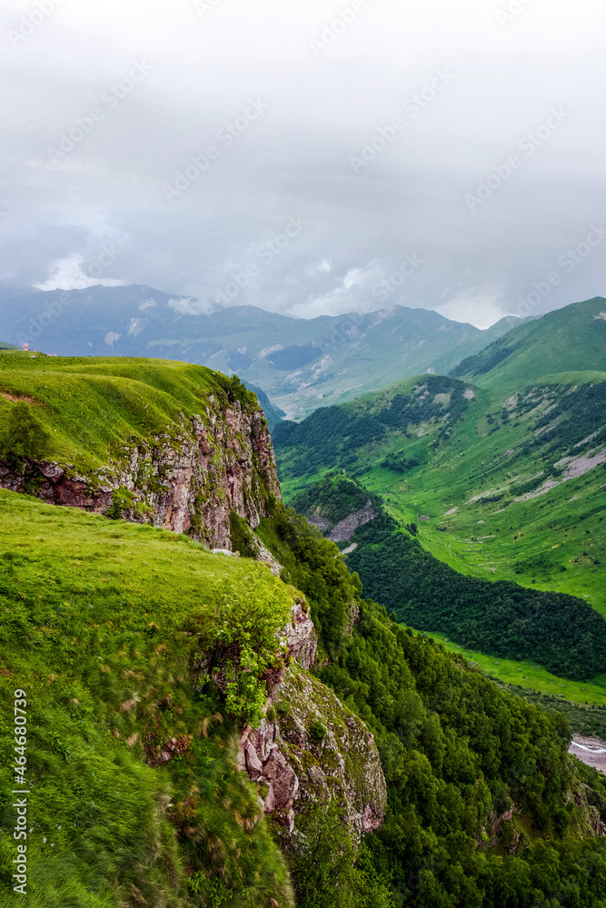 Naklejka premium Kazbegi Mountains. View from the mountain to the city, the village of Stepantsminda. Green hills, mountain peaks. Travel in the mountains of Georgia.