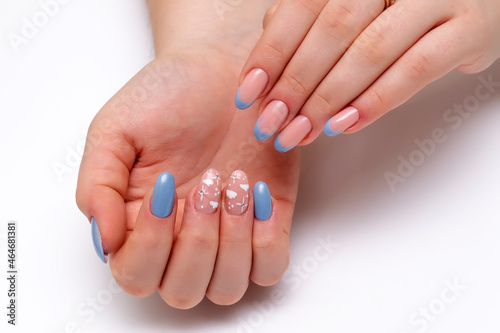 Blue French manicure with painted clouds and crystals on a close-up of long oval nails on a white background. Gel nails.
