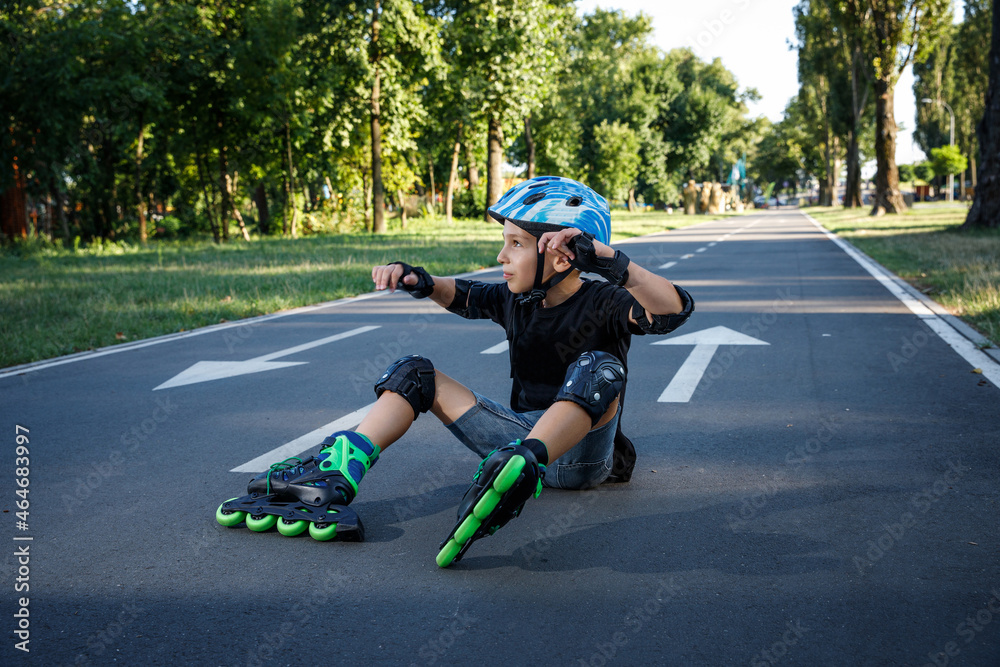 The boy is rollerblading on the track in the city park. The child learns to roller-skate. An active walk with a child on the street.The boy fell on the asphalt on roller skates.