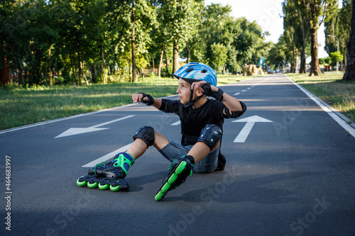 The boy is rollerblading on the track in the city park. The child learns to roller-skate. An active walk with a child on the street.The boy fell on the asphalt on roller skates. © Анна Кондратенко