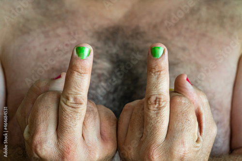 Close-up with selective focus of male fingers with green painted nails doing the sign to fuck off.