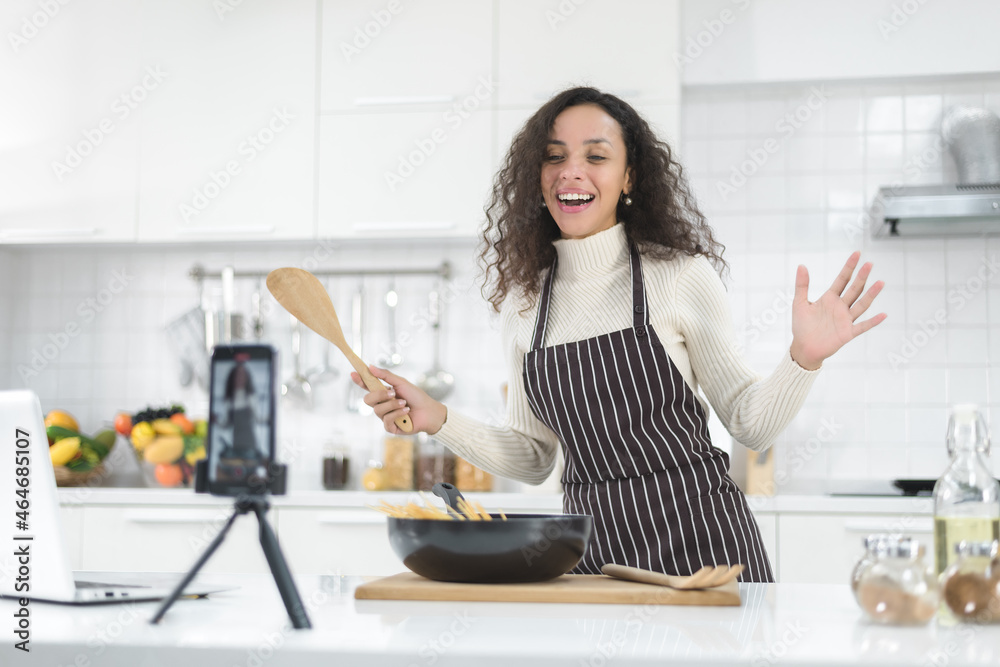 Latin women live streaming online with a smartphone while cooking in the kitchen at home. Latin women live streaming online with a smartphone while cooking in the kitchen at home.