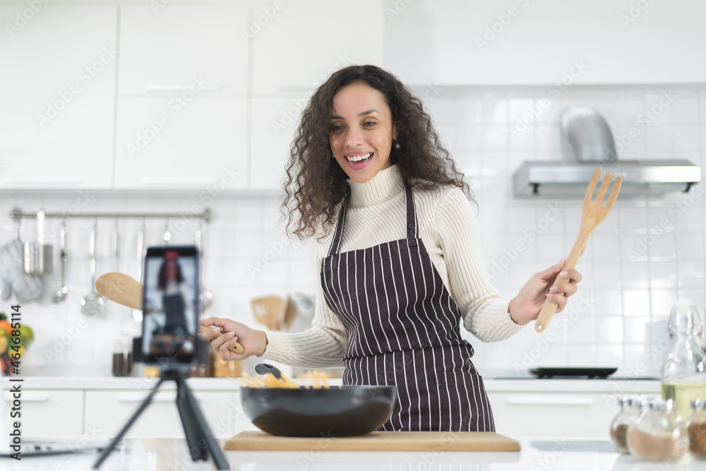 Latin women live streaming online with a smartphone while cooking in the kitchen at home. Latin women live streaming online with a smartphone while cooking in the kitchen at home.