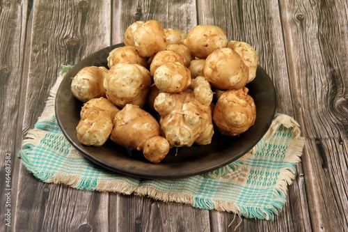 Raw Jerusalem artichoke in a clay bowl on wooden boards background. Raw Organic topinambour