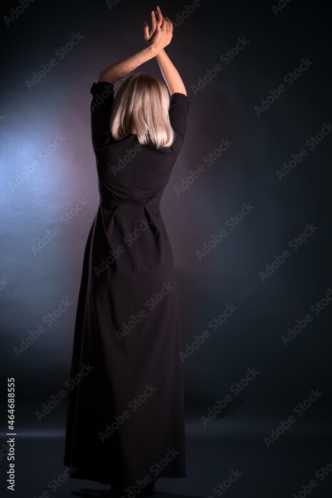 Woman with long hair stands with her back to the viewer and holds her hands above her head
