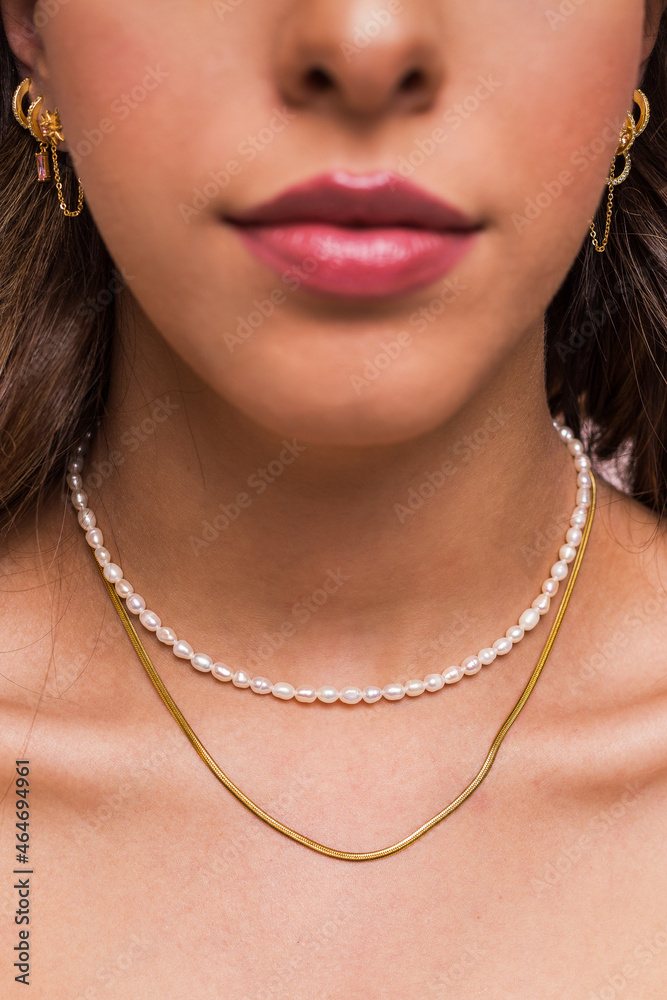 Beautiful young woman wearing a pearl necklace and a snake chain and gold earings hang from woman's ear