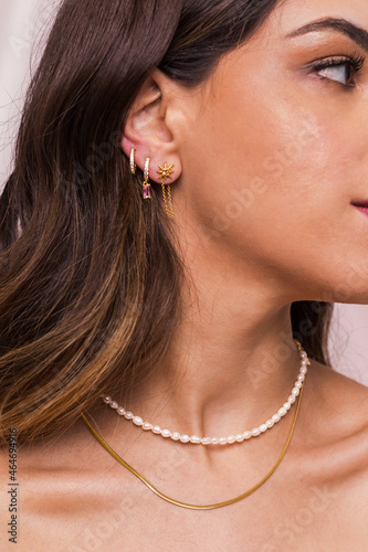 Beautiful young woman's neck wearing a pearl necklace and a snake chain and gold earings hang from woman's ear