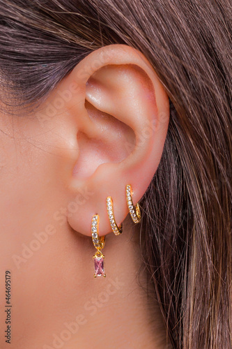 Woman ear with mulriple piercings wearing beautiful earrings with zirconia