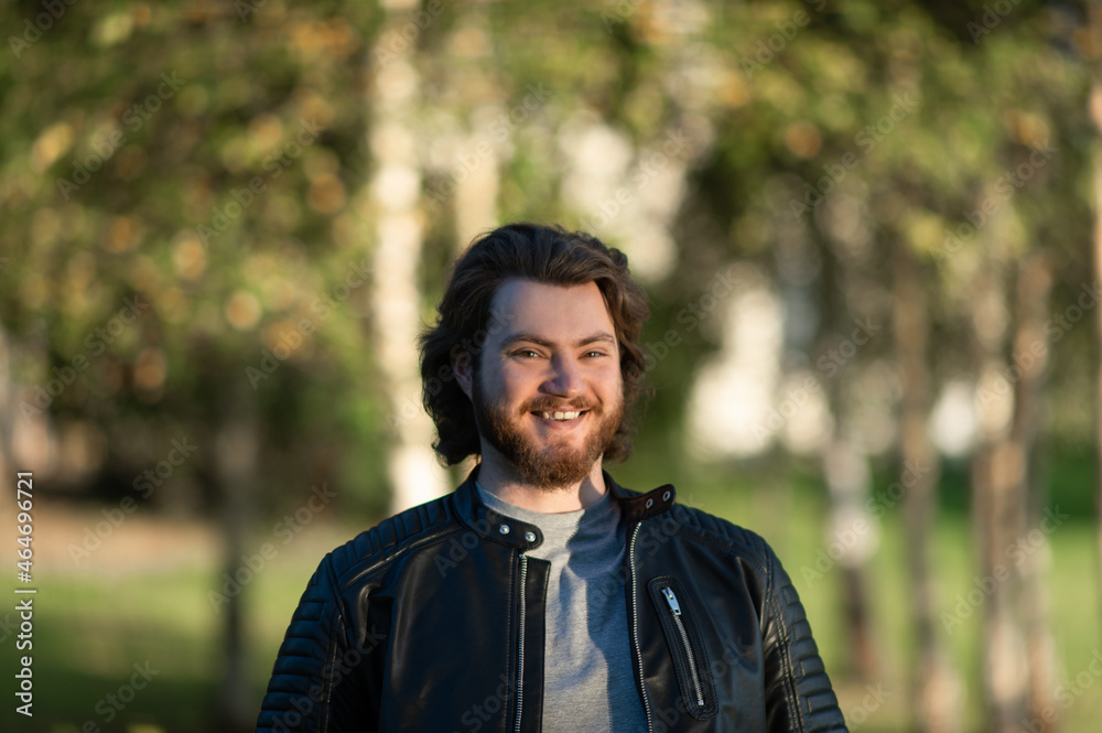 happy young bearded man smiling and looking to camera against autumn color trees background happy young bearded man smiling and looking to camera against autumn color trees background