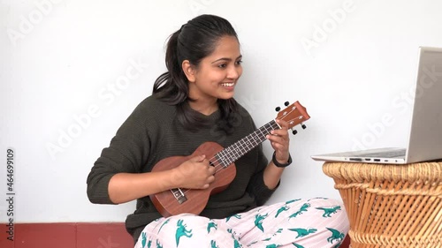 Young woman playing ukulele in front of a laptop. Concept of online learning and teaching	