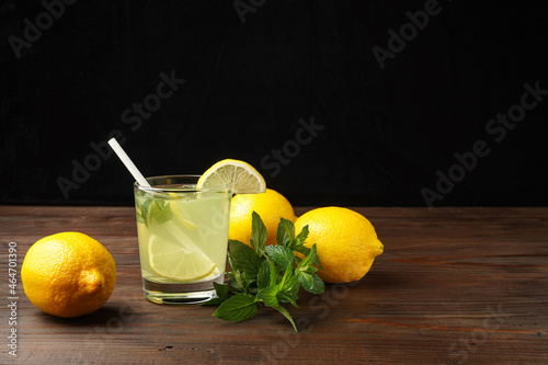 Lemonade or mojito cocktail with lemon and mint, cold refreshing drink or beverage with ice on rustic wood background. Homemade lemon and ginger organic drink, copy space.