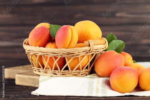 Sweet apricots in basket and napkin on brown wooden background