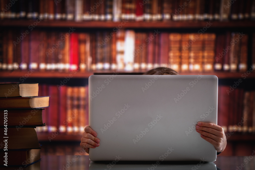Young beautiful child girl working  with laptop and reading books in library. Horizontal image. Selective focus on hands.