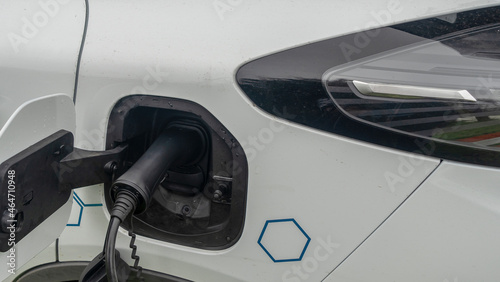 Close-up view of power supply plugged into an electric car being charged. White electric car charging.