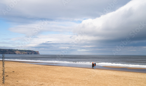 Unidentifiable couple walking along a deserted sandy beach on a dull and overcast autumn day in the coastal town of Whitby, North Yorkshire