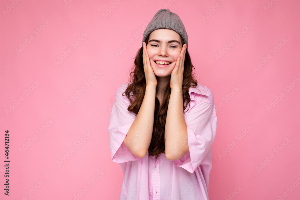 Portrait of beautiful positive cheerful cute smiling young brunette woman in stylish shirt and hipster grey hat isolated on pink background with copy space