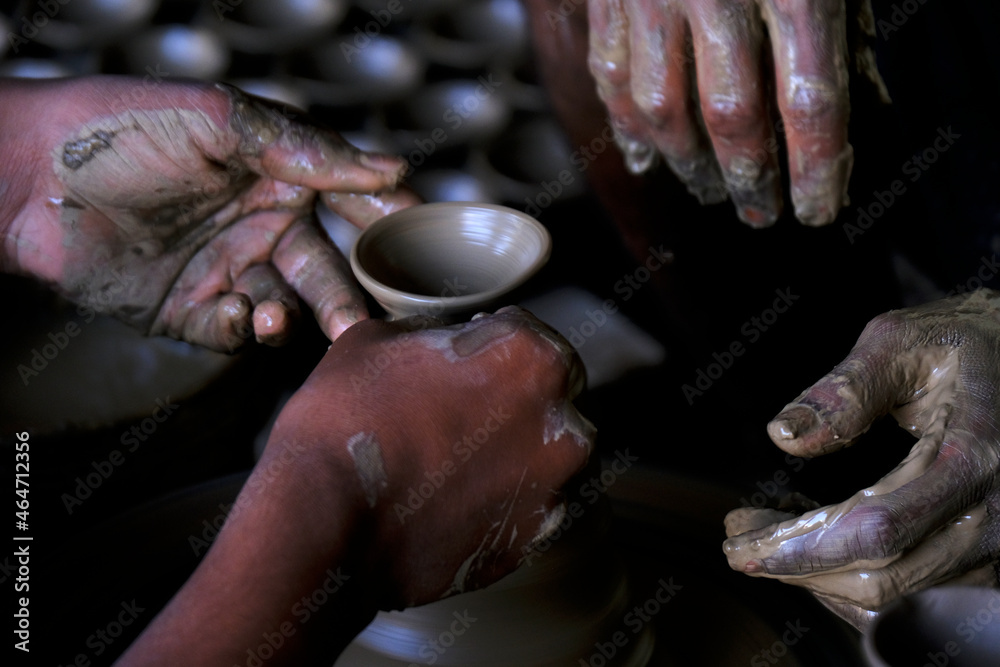 A potter prepares clay Pots or diya on potter's wheel in his residence ahead of Diwali festival. Wet and muddy hands of a craftsman shaping a clay vase on a pottery wheel.