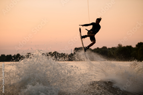 Fototapeta Naklejka Na Ścianę i Meble -  active guy jumping over splashing wave on wakeboard holding on to the rope. Water sports activity.