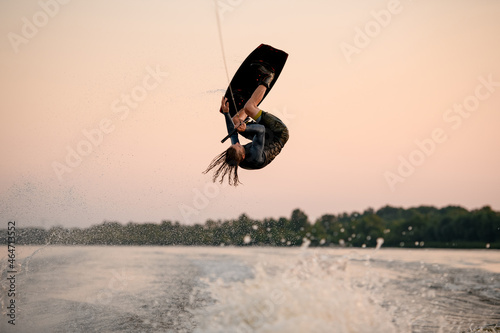 male wakeboarder makes dangerous stunts jumping and flips on wakeboard over splashing wave photo