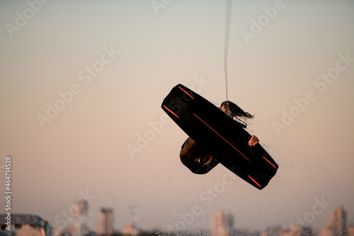 gorgeous view of man making extreme stunts jumping and flips on wakeboard against the backdrop of sky