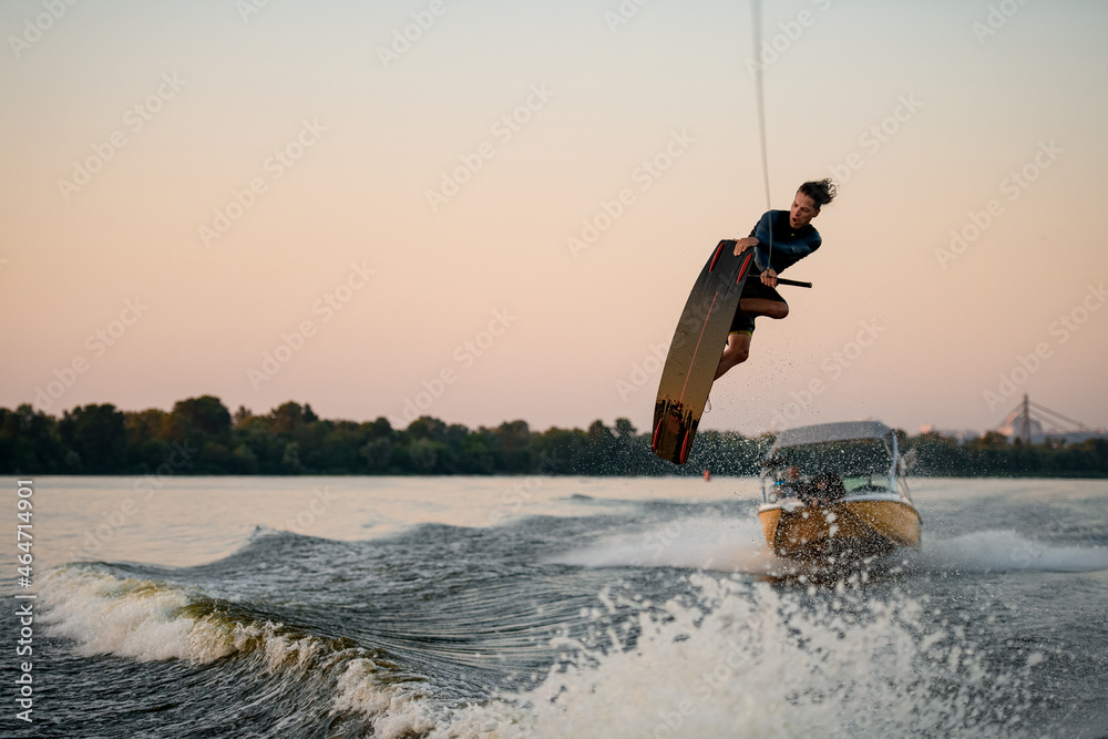Athletic man having fun and jumping on splashing wave on a wakeboard