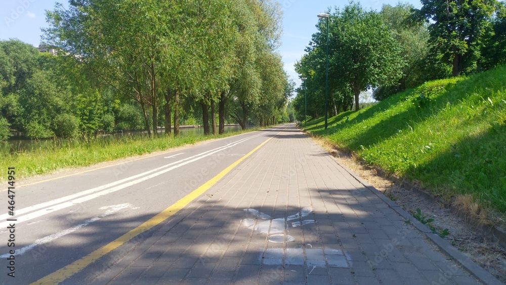 Trees grow along the riverbed that flows through the city, and paved bicycle and tiled pedestrian paths are laid, on which markings are applied. There are lighting poles along them.