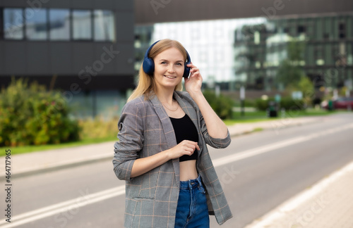 Portrait of young happy woman listening to music with headphones and smiling while walking on the street in the city. Music lover enjoying music. Portrait of businesswoman walking and smiling outdoor