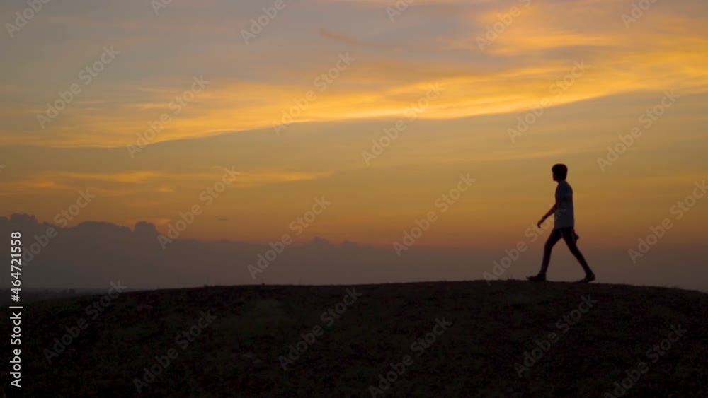 Silhouette of a defocused Indian man walking in front of the orange clouds after the sunset during the blue hour. Selective Focus in the Sky. Lonely man walks in front of the orange clouds. Silhouette of a defocused Indian man walking in front of the orange clouds after the sunset during the blue hour. Selective Focus in the Sky. Lonely man walks in front of the orange clouds.