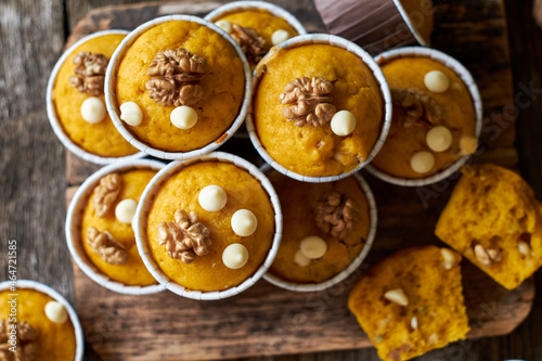 Pumpkin muffins with white chocolate and walnuts. Top view, wooden background.