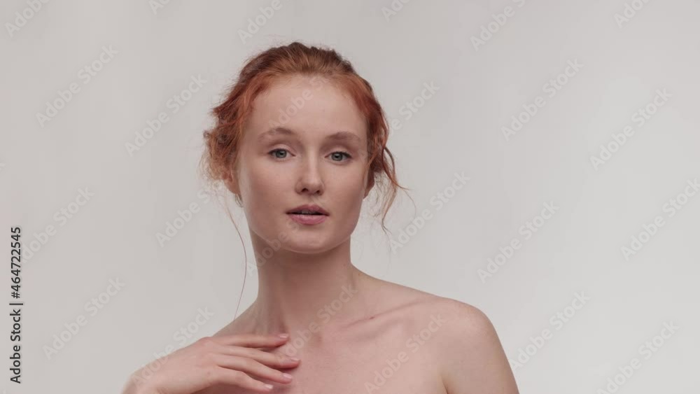 Slow motion beauty portrait of young ginger woman touching her smooth skin in collarbone area. Skin care concept. Female model with fresh skin, white smile and natural facial makeup portrait. Close up Slow motion beauty portrait of young ginger woman touching her smooth skin in collarbone area. Skin care concept. Female model with fresh skin, white smile and natural facial makeup portrait. Close up