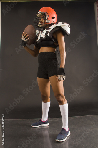 young woman with american football shoulder pads and ball, full length