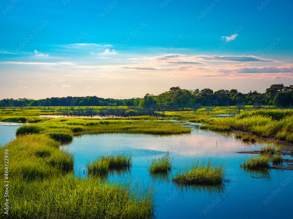 Cape Cod marshland seascape with circularly scattered little islands of wild plants.  Tranquil curving river flowing through the swampy marshland on Cape Cod at full tide. Vibrant colors of the green 