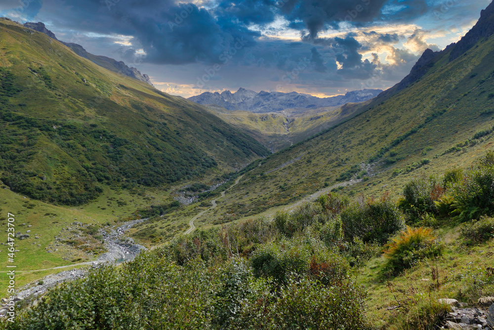 Fototapeta premium Green valley with a footpath and a mountain stream, high above Gargellen, Vorarlberg, Austria, in the high Alps, under a dark evening sky 