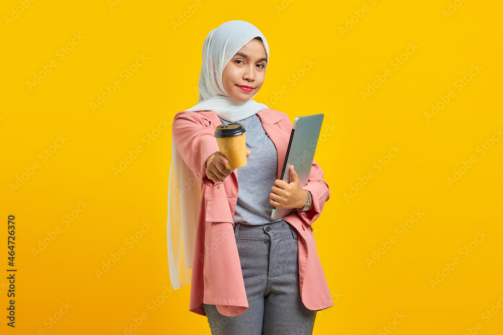 Portrait of cheerful young Asian woman holding laptop and coffee isolated over yellow background