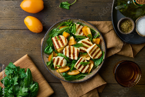 Vegetarian salad with vegetable, greenery, dairy and nuts. Summer lunch with fresh spinach, grilled circassian halloumi cheese, sliced orange tomatoes, olive oil and spices. Horizontal, flat lay photo