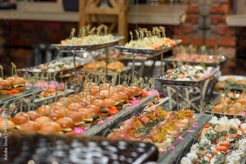 A set of canapes and snack at a banquet with white table. Slices of tomato, olive, cheese, bread and fish on food stand
