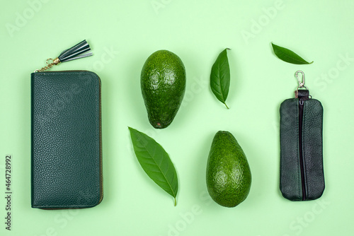 Wallet and avocado on green background. Concept of faux leather made from avocado peel skin, products alternative instead of animal skins, eco vegan leather, sustainable innovative materials