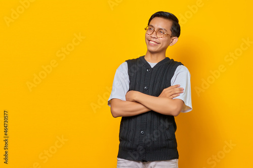 Portrait of smiling Asian young man with crossed arms isolated on yellow background