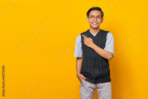 Portrait of smiling young Asian man pointing to copy space with finger