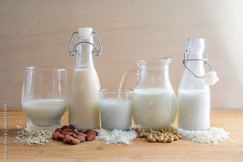 Vegan milk variations made from cereals and nuts in glasses and bottles with ingredients, alternative to animal dairy products on a wooden table, copy space Vegan milk variations made from cereals and nuts in glasses and bottles with ingredients, alternative to animal dairy products on a wooden table, copy space