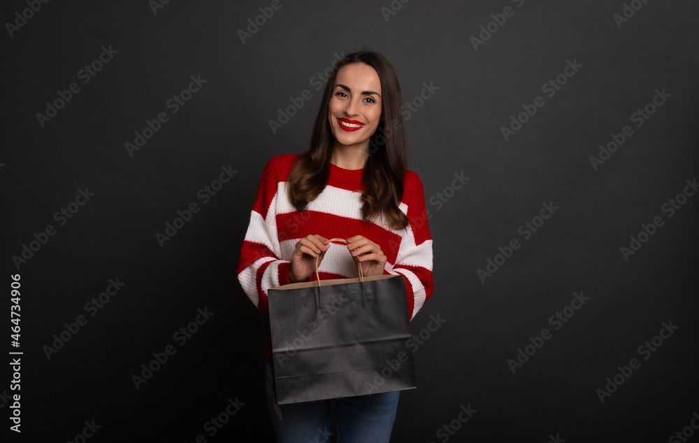 Close up photo of gorgeous smiling stylish brunette woman with black shopping bag in hands while she isolated on gray background Close up photo of gorgeous smiling stylish brunette woman with black shopping bag in hands while she isolated on gray background