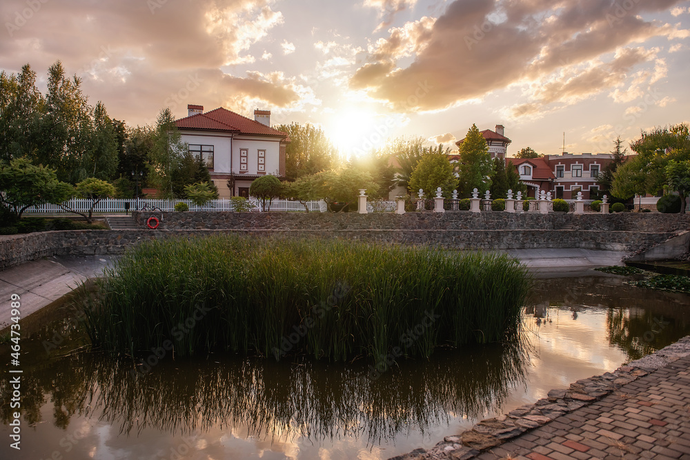 Obraz premium Panoramic view of the cottage village by the pond with green reeds at sunset. Life outside the city
