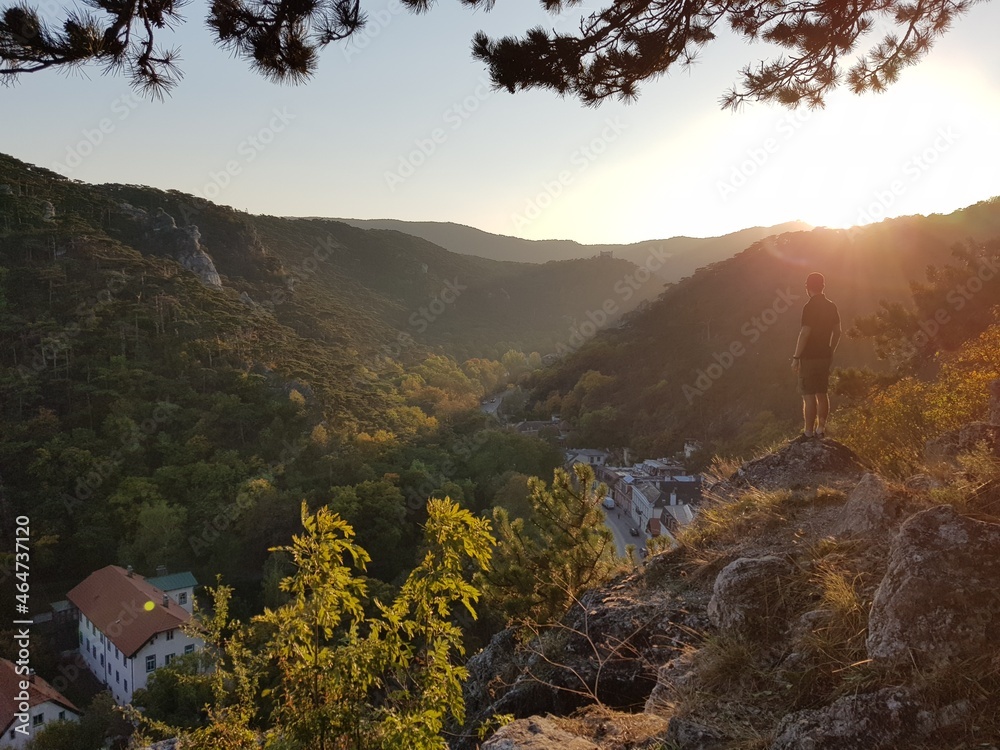 Fototapeta premium Young sporty male hiker is looking on sunset in the mountains and enjoy life. Freedom, hiking and traveling in the wild nature. Beautiful background image. Active lifestyle, Travel and Holiday concept