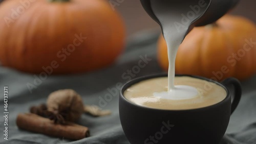 Slow motion making spiced pumpkin latte in black cup, pour steamed milk photo