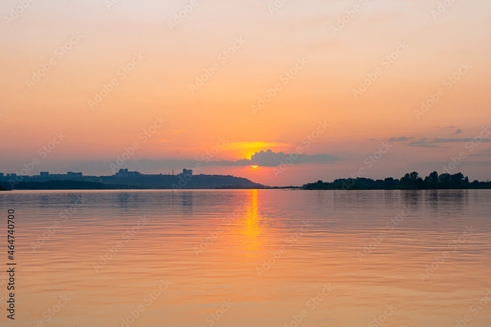 Calm water surface with pink sunset sky and sun through the clouds over. Meditation water and yellow sky background. Horizon over the water. Calm water surface with pink sunset sky and sun through the clouds over. Meditation water and yellow sky background. Horizon over the water.