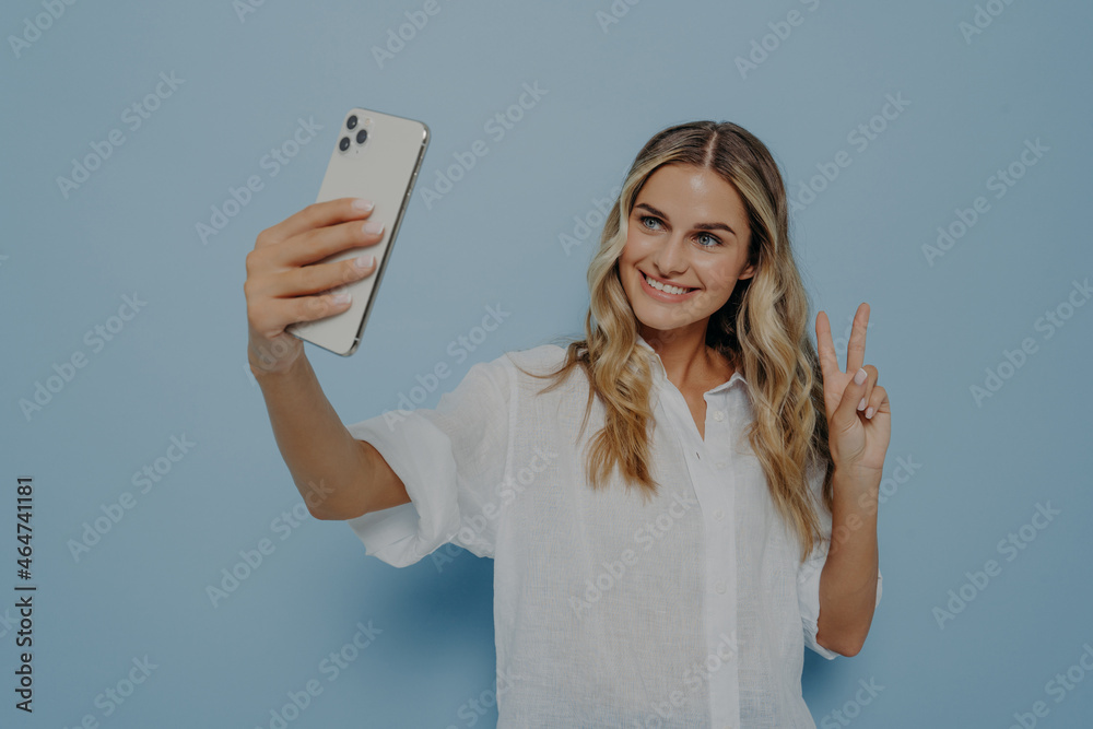 Blonde teenage girl showing peace sign while taking selfie on smartphone Blonde teenage girl showing peace sign while taking selfie on smartphone