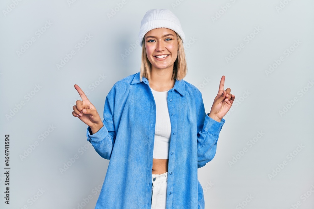 Beautiful blonde woman wearing wool hat smiling confident pointing with fingers to different directions. copy space for advertisement Beautiful blonde woman wearing wool hat smiling confident pointing with fingers to different directions. copy space for advertisement