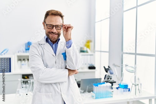 Middle age hispanic man wearing scientist uniform standing at laboratory